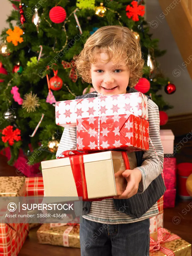 Young child holding gifts in front of Christmas tree