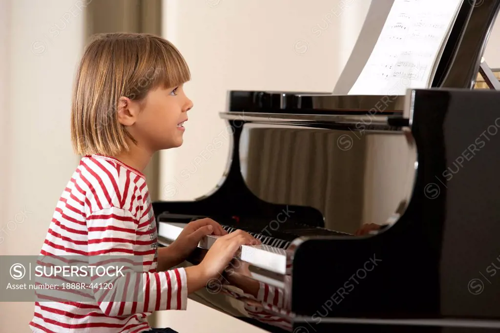 Young girl playing grand piano at home