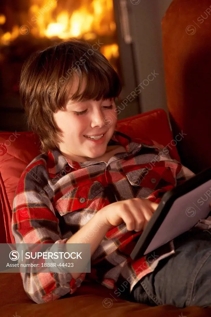 Young Boy Relaxing With Tablet Computer By Cosy Log Fire