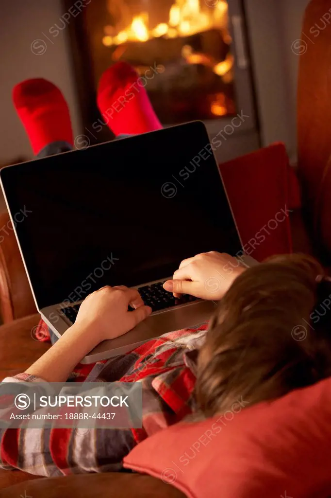 Young Boy Relaxing With Laptop By Cosy Log Fire