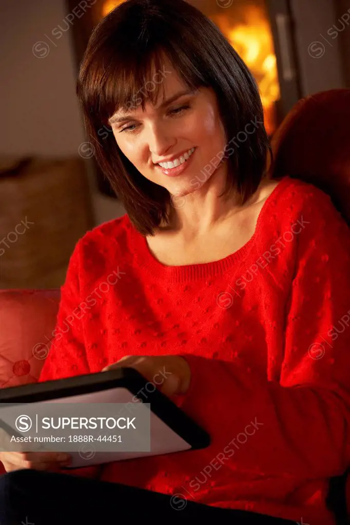 Middle Aged Woman Using Tablet Computer By Cosy Log Fire