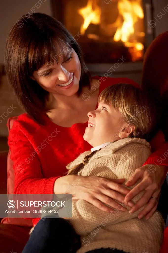 Mother And Daughter Relaxing On Sofa By Cosy Log Fire