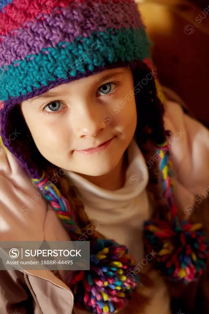 Young Girl Sitting On Wooden Seat Wearing Warm Outdoor Clothes