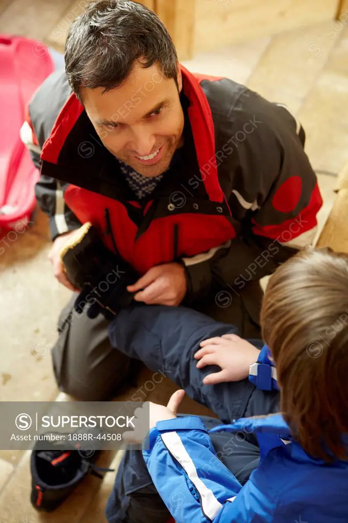 Father Helping Son To Put On Warm Outdoor Clothes And Boots