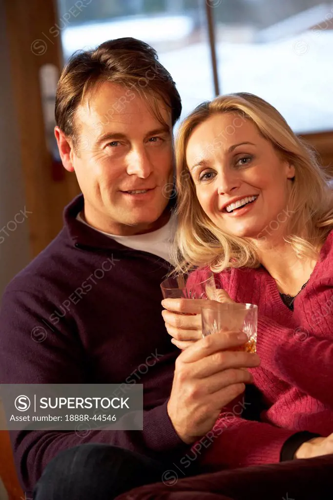 Middle Aged Couple Sitting On Sofa With Glasses Of Whisky