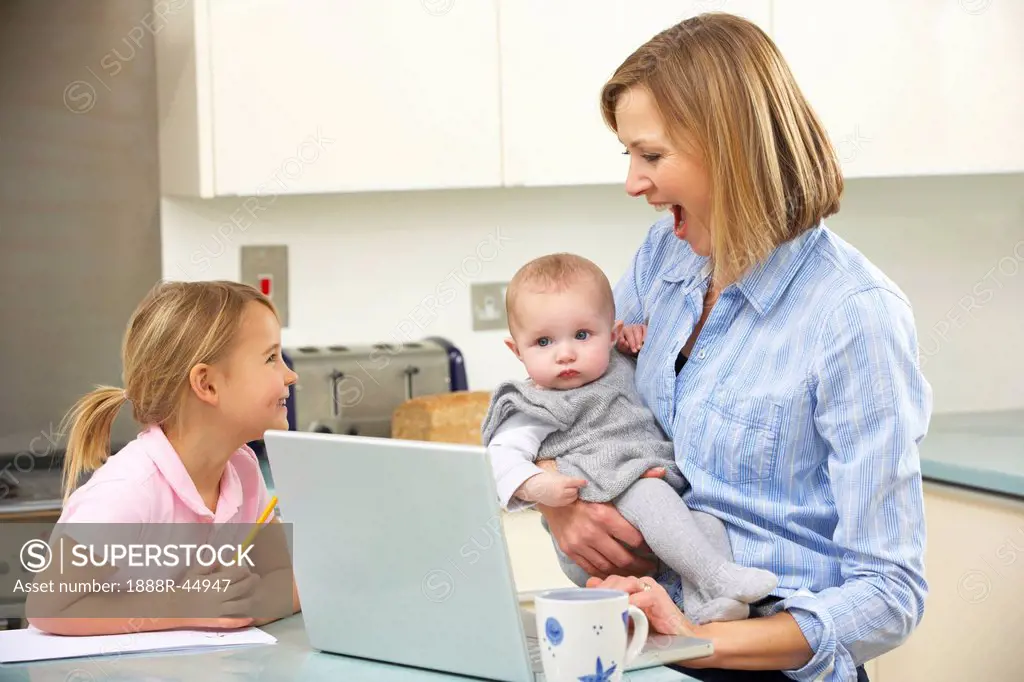 Mother with children using laptop in kitchen