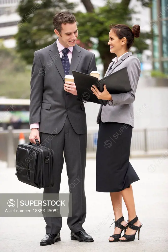 Businessman And Businesswoman Discussing Document In Street Holding Takeaway Coffee