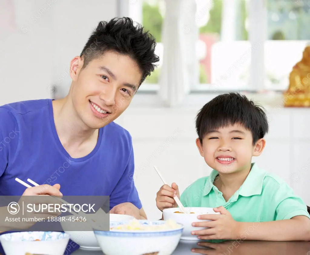 Chinese Father And Son Sitting At Home Eating A Meal