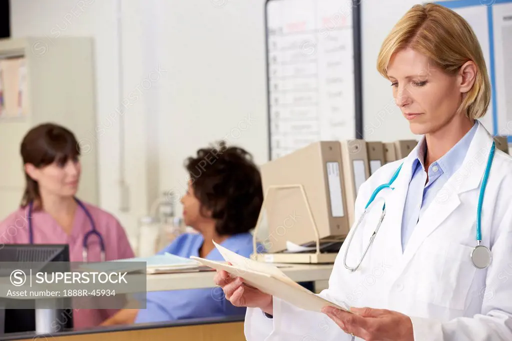 Female Doctor Reading Patient Notes At Nurses Station