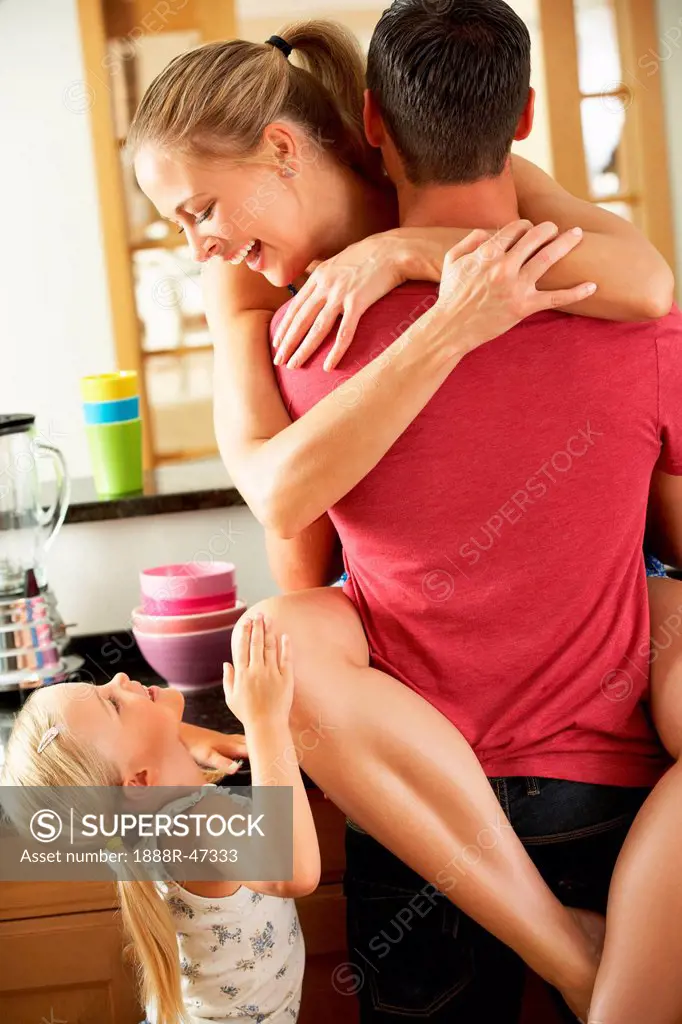 Romantic Couple Hugging In Kitchen Being Interrupted By Daughter