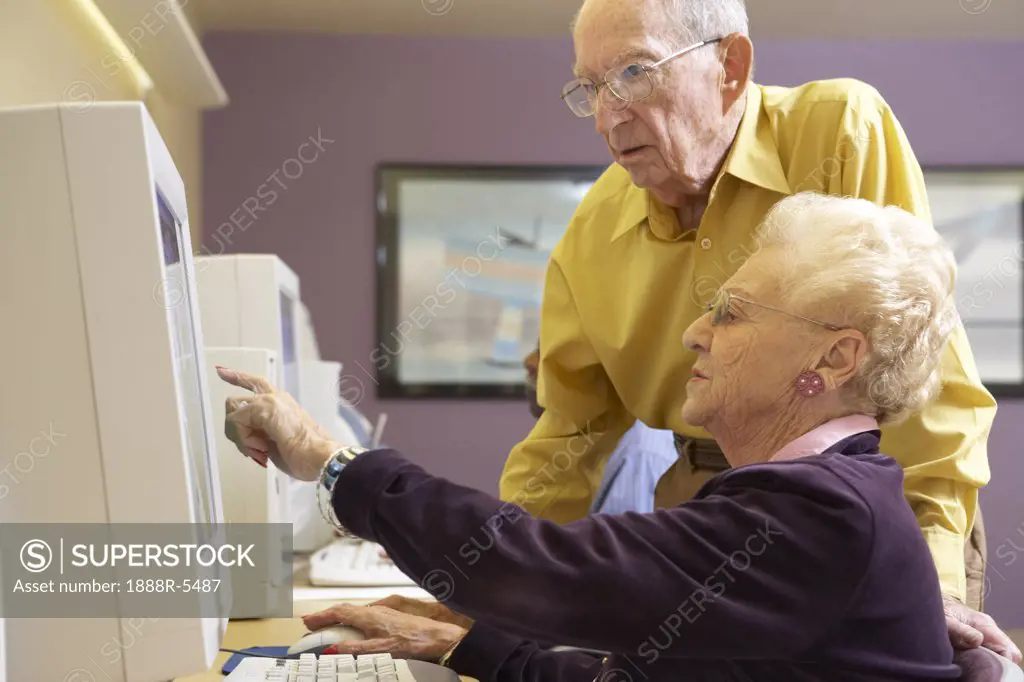 Senior man helping senior woman to use computer