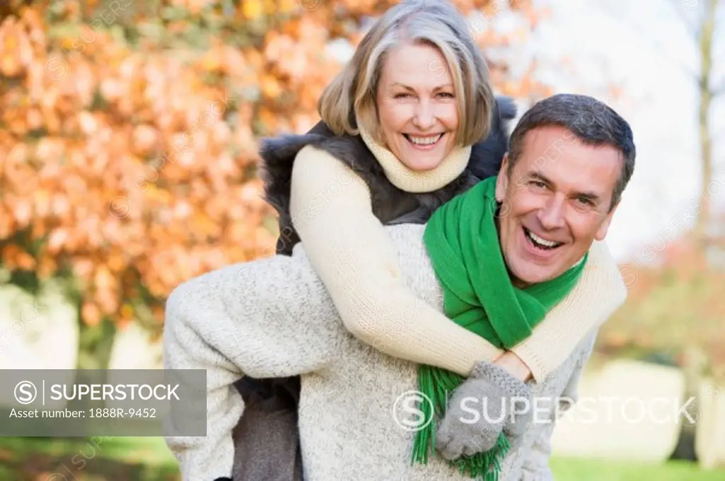 Senior man outdoors piggybacking woman and smiling selective focus
