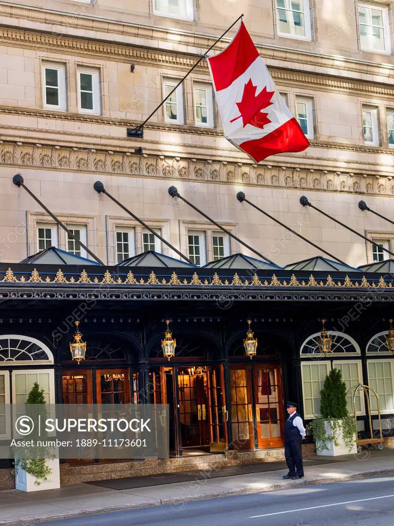 A valet stands outside the entrance of a hotel with a Canada flag flying overhead; Montreal, Quebec, Canada