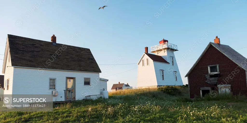 Houses and a lighthouse on the Atlantic coast; North Rustico, Prince Edward Island, Canada