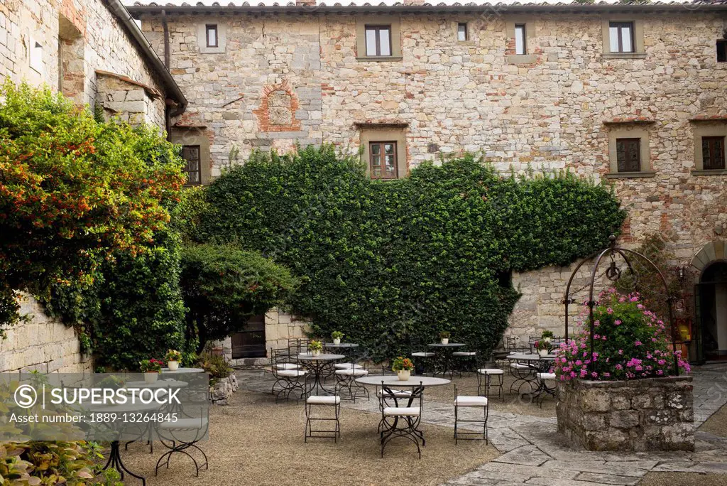 Courtyard filled with tables and chairs, vines and shrubs growing around stone buildings; Gaiole in Chianti, Toscana, Italy