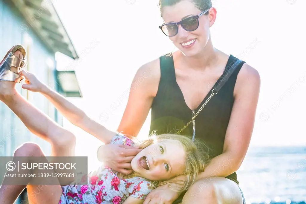 Portrait of a mother and daughter sitting together while on vacation in Lahaina along Front Street in bright sunlight with the Pacific Ocean in the ba...