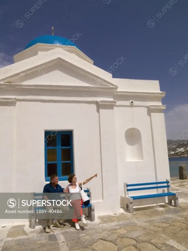 Senior couple sitting outside orthodox church; Mykonos, Greece