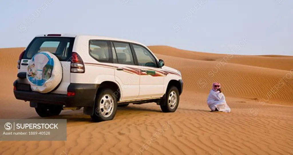 Bedu guide waiting by car; Wahiba, Oman