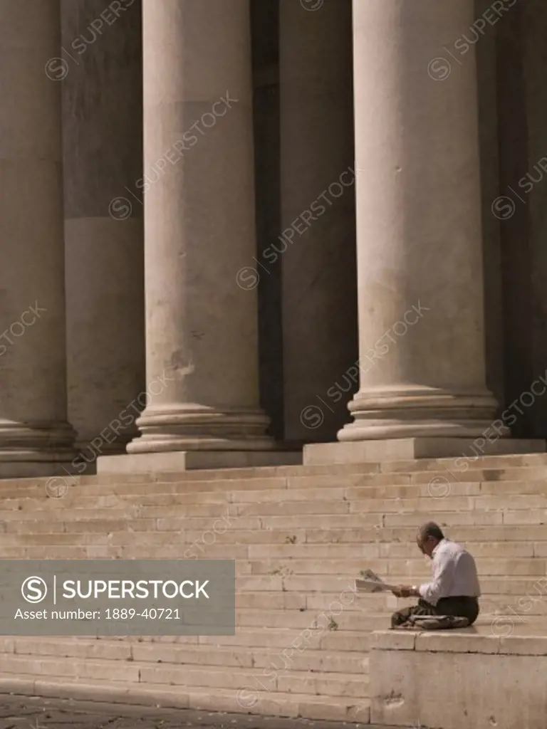Man readning newspaper, stairs with columns in background; Naples, Italy