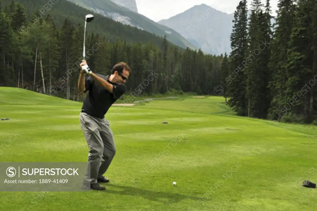 Mid-adult man playing golf; Canmore, Alberta's Rockies, Alberta, Canada