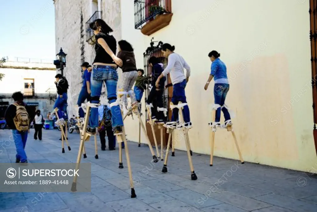 Teenage girls walking on stilts on street; Mexico