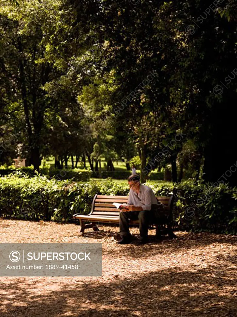 Mid-adult man reading book in public park near Villa Borghese; Rome, Italy