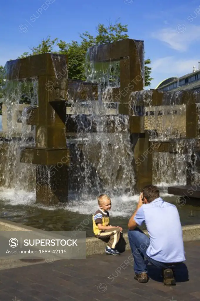 Father photographing son at Waterfront Park Fountain; Seattle, Washington State, USA