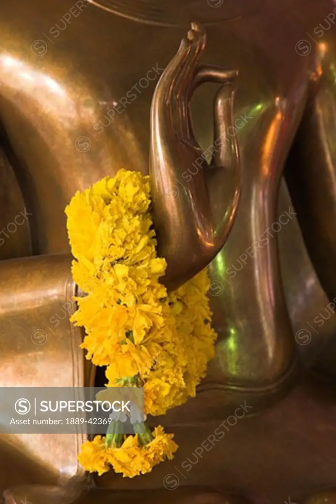 Wat Somdej Phuttachan, Thailand; Close-up of flowered lei over hand of Buddhist statue