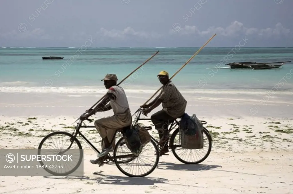 Pwani Mchangani, Zanzibar, Tanzania; Men cycling holding poles