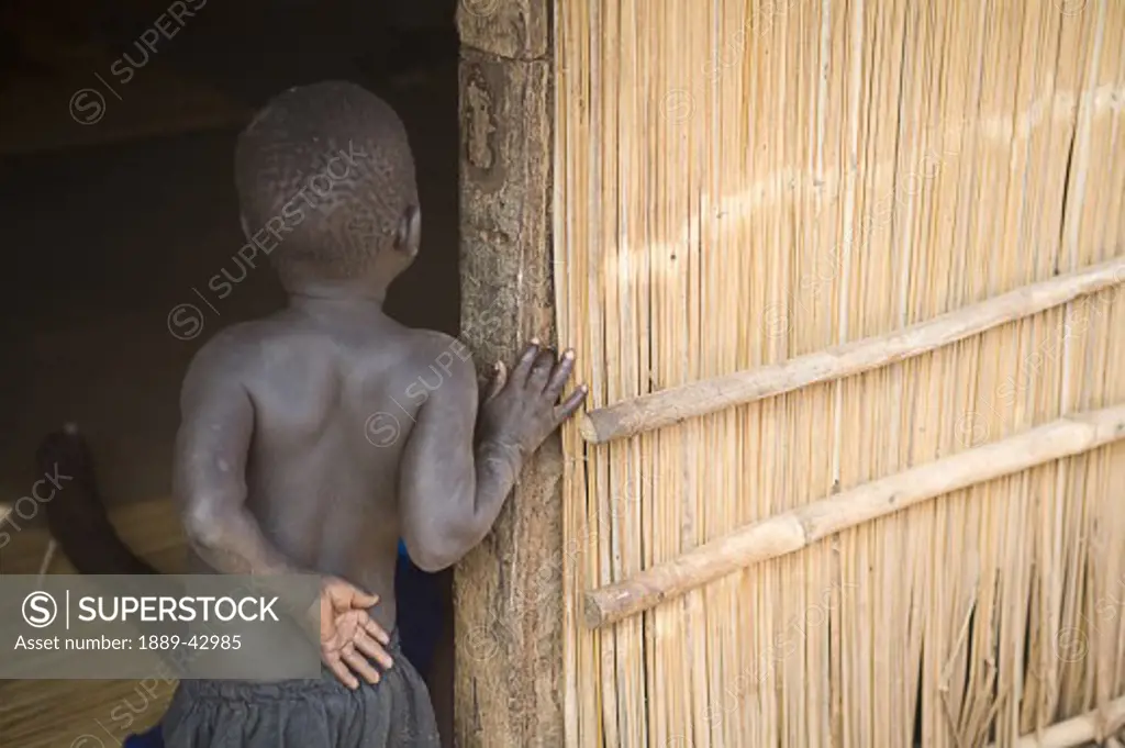 Gulu, Northern Uganda; Young boy looking around door into house