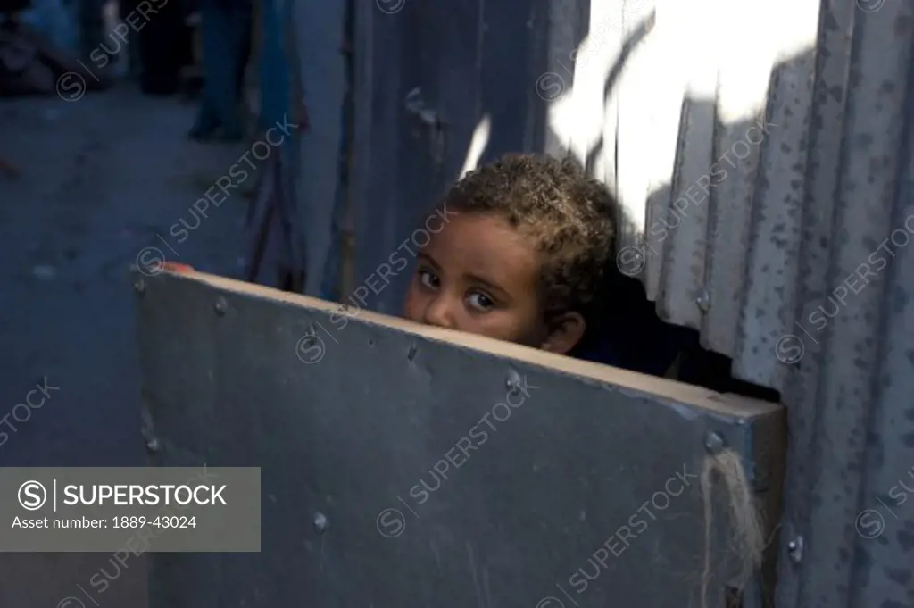 Ethiopia; Young boy looking over corrugated iron door