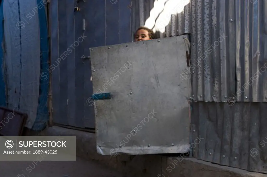 Ethiopia; Young boy looking over corrugated iron door in wall