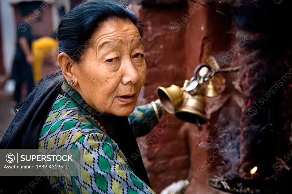 Boudhnath, Kathmandu, Nepal; Woman ringing bells in street