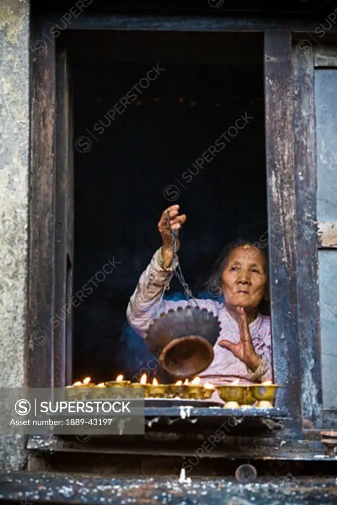 Boudhnath, Kathmandu, Nepal; Woman swinging incense bowl over candles