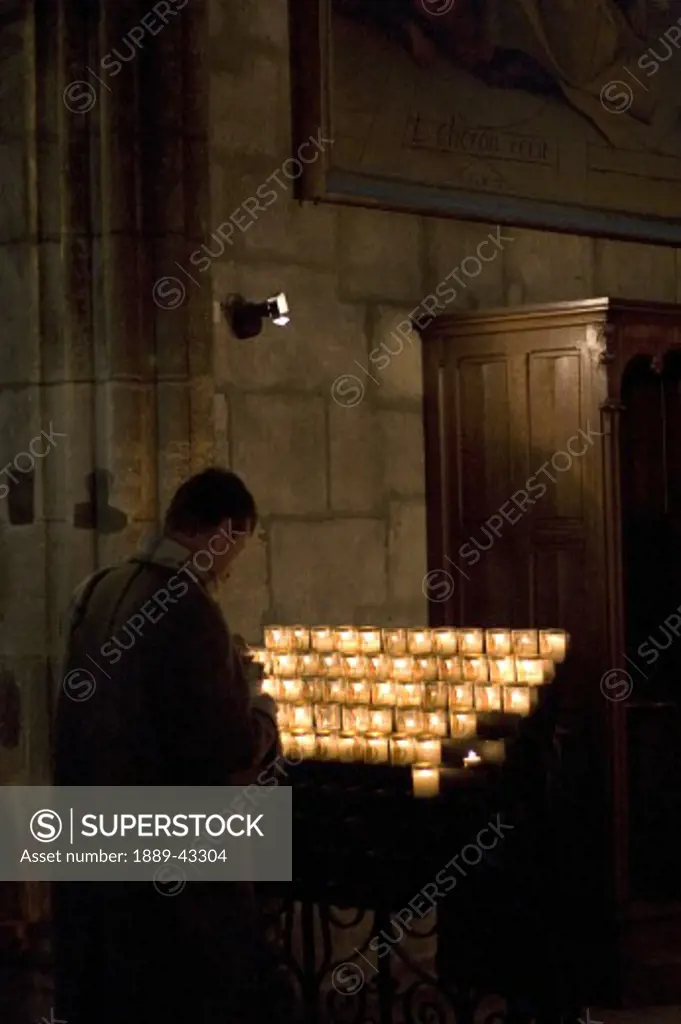 Paris, France; A man lighting a candle in a church