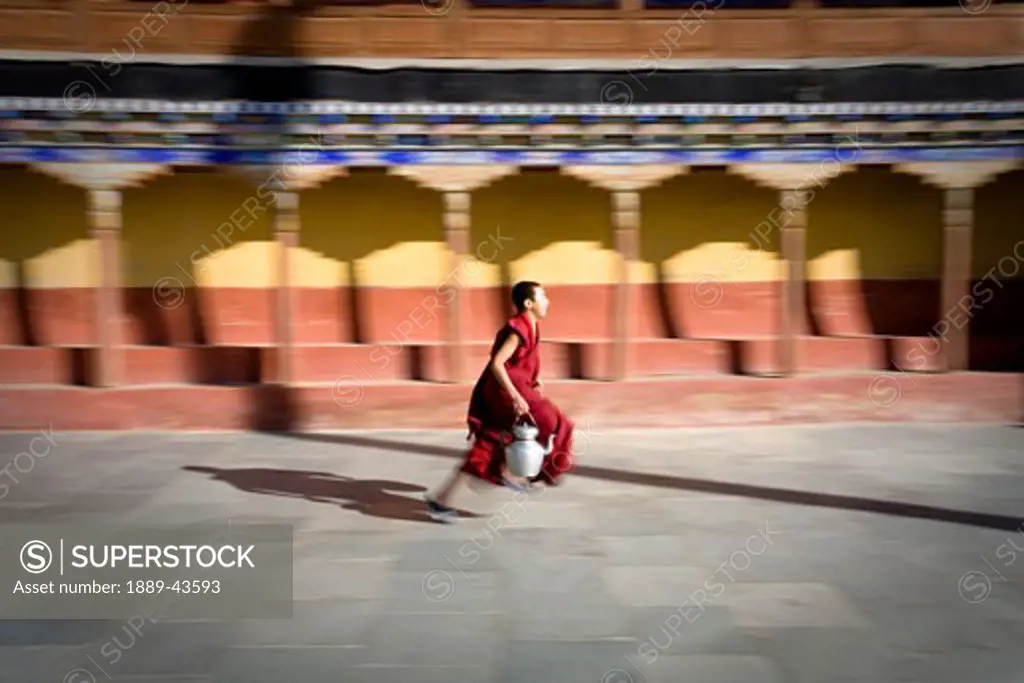 Thiksey Gompa, Ladakh, Jammu and Kashmir, India; Buddhist student running through monastery carrying teapot