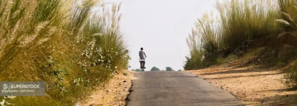 Rajasthan,India;Boy riding his bike along a rural road