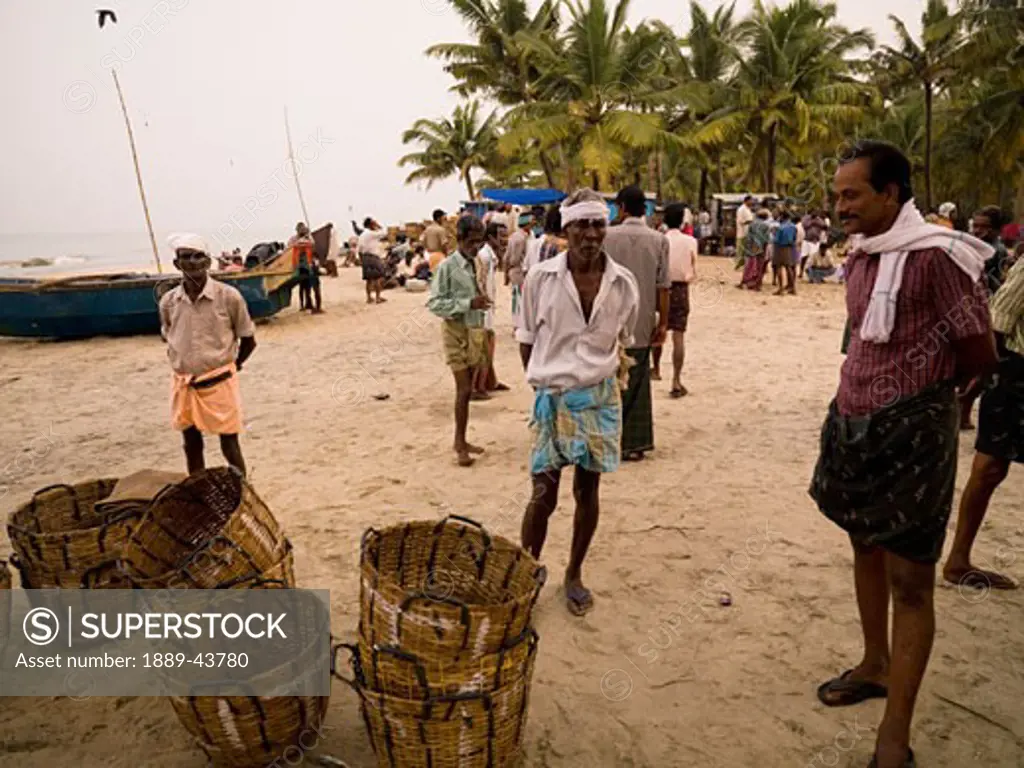 Kerala,India;Fishermen standing on beach next to fishing basket