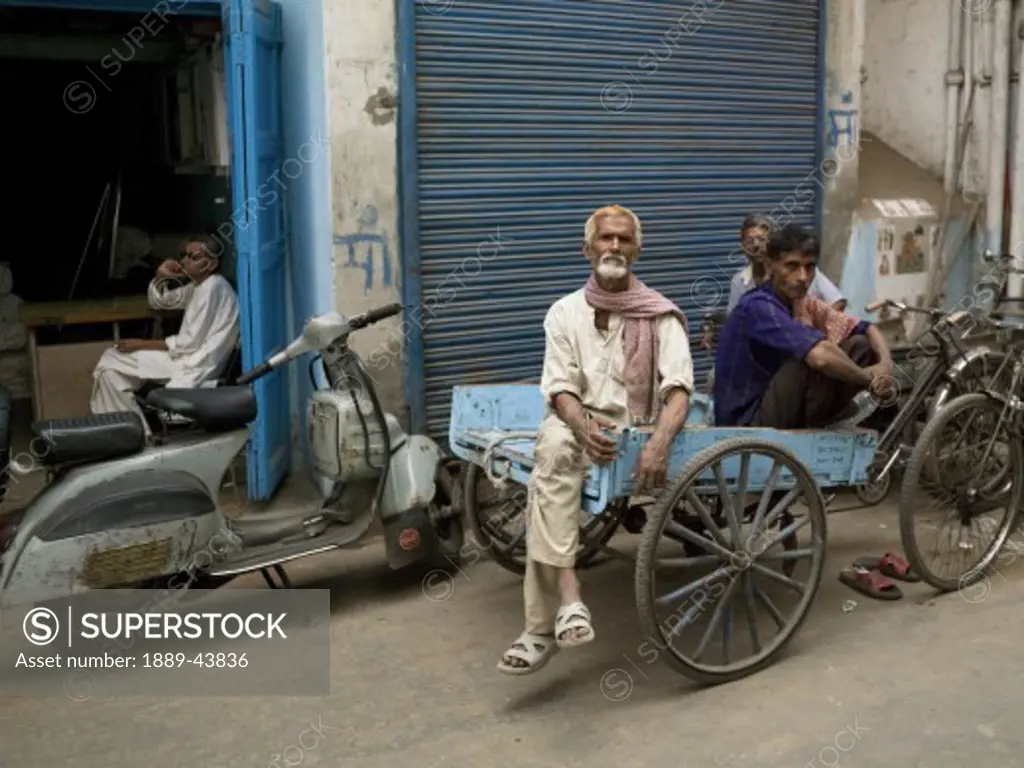 Delhi,India;Men sitting on a cart outside shop front