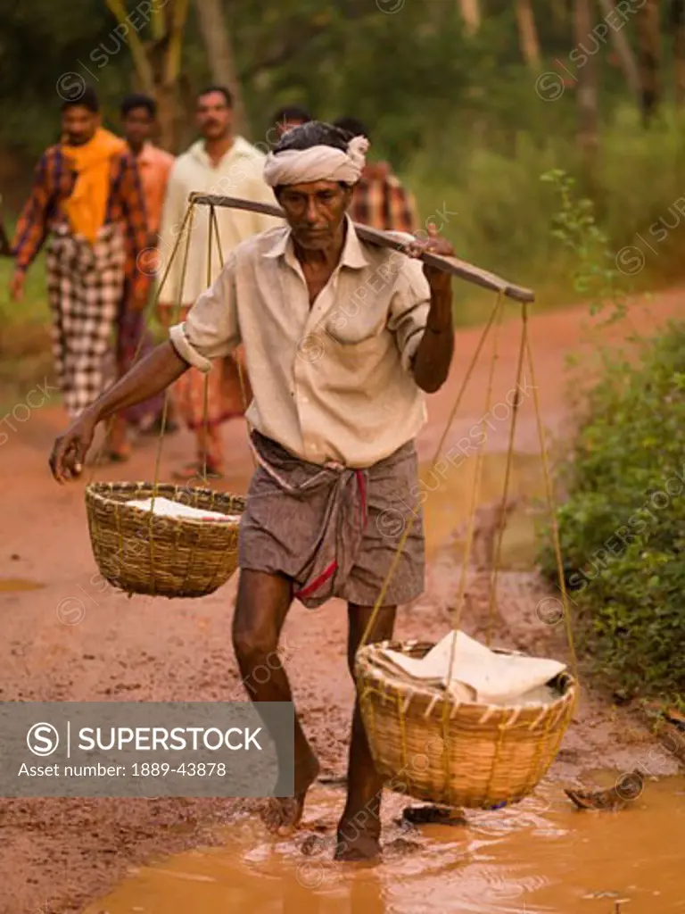 Kerala,India;Fisherman carrying baskets along mud road