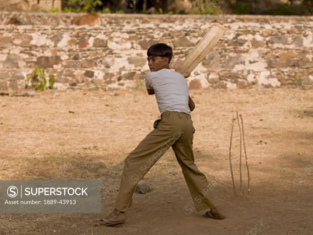 Aravalli Hills,Rajasthan,India;Aravalli Hills,Rajasthan,India;Boy playing cricket,using makeshift equipment 