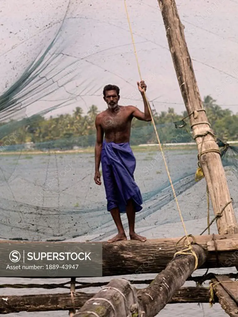 Kochi,Kerala,India;Fisherman stands alongside Chinese fishing nets