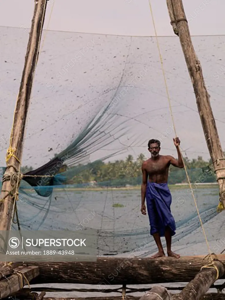 Kochi,Kerala,India;Fisherman stands alongside Chinese fishing nets