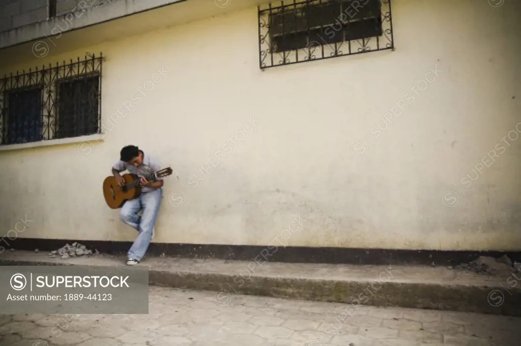 Patzicia,Guatemala;Man leaning against a wall playing guitar