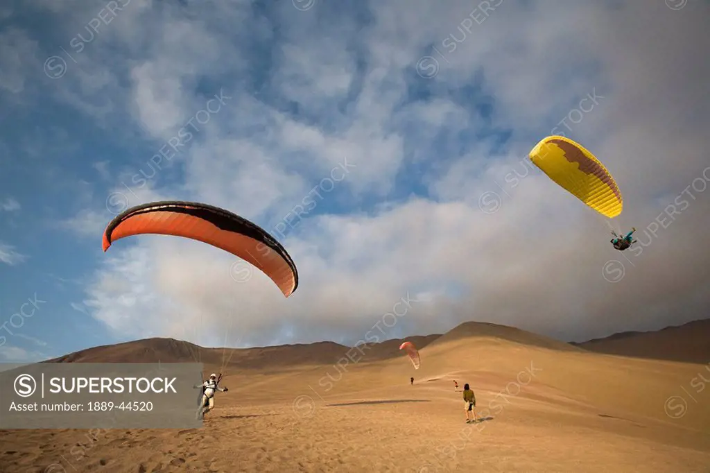 Three people parasailing and landing in the desert