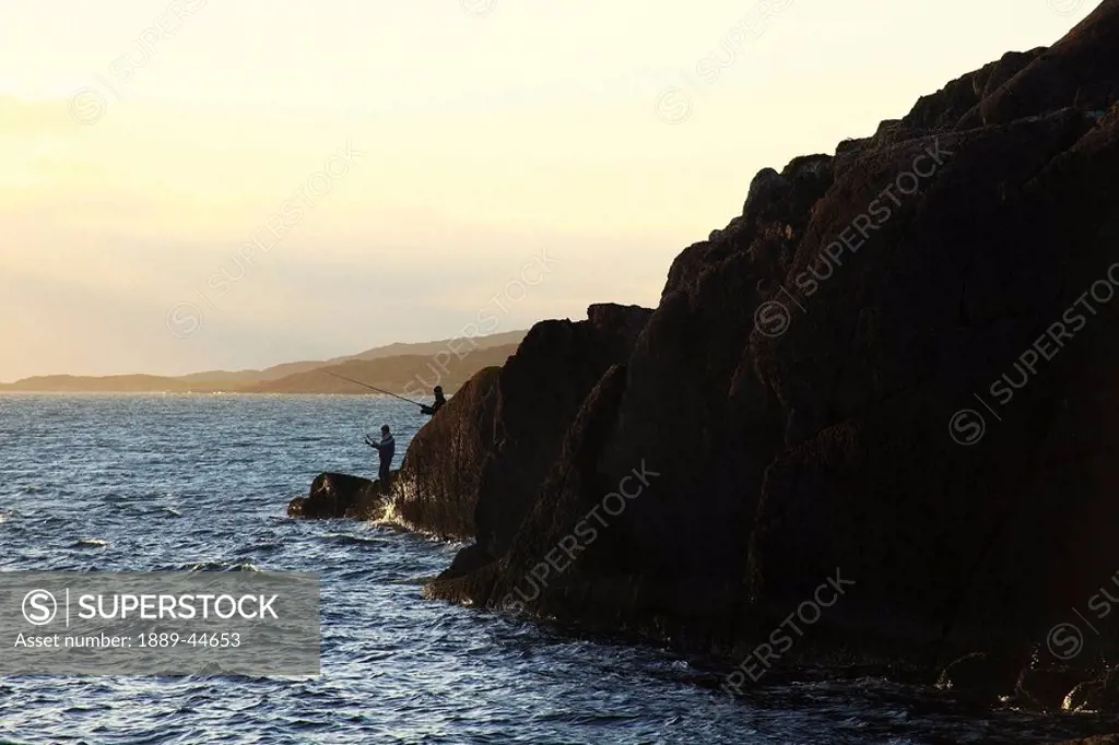 Two people fishing off a hillside