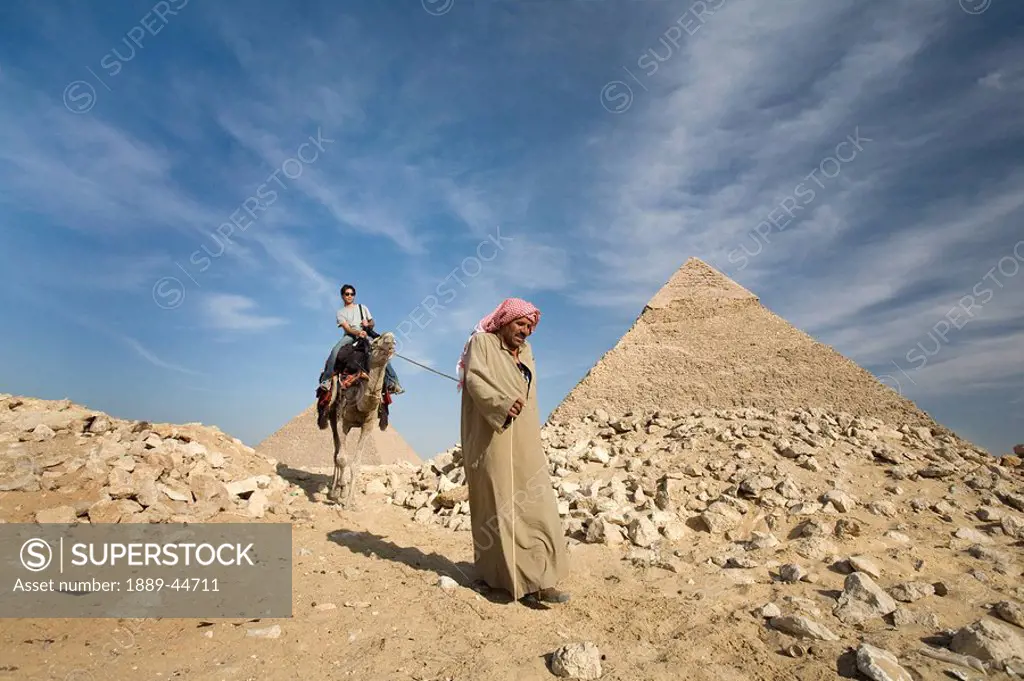 A guide leading a camel and passenger by the Pyramids
