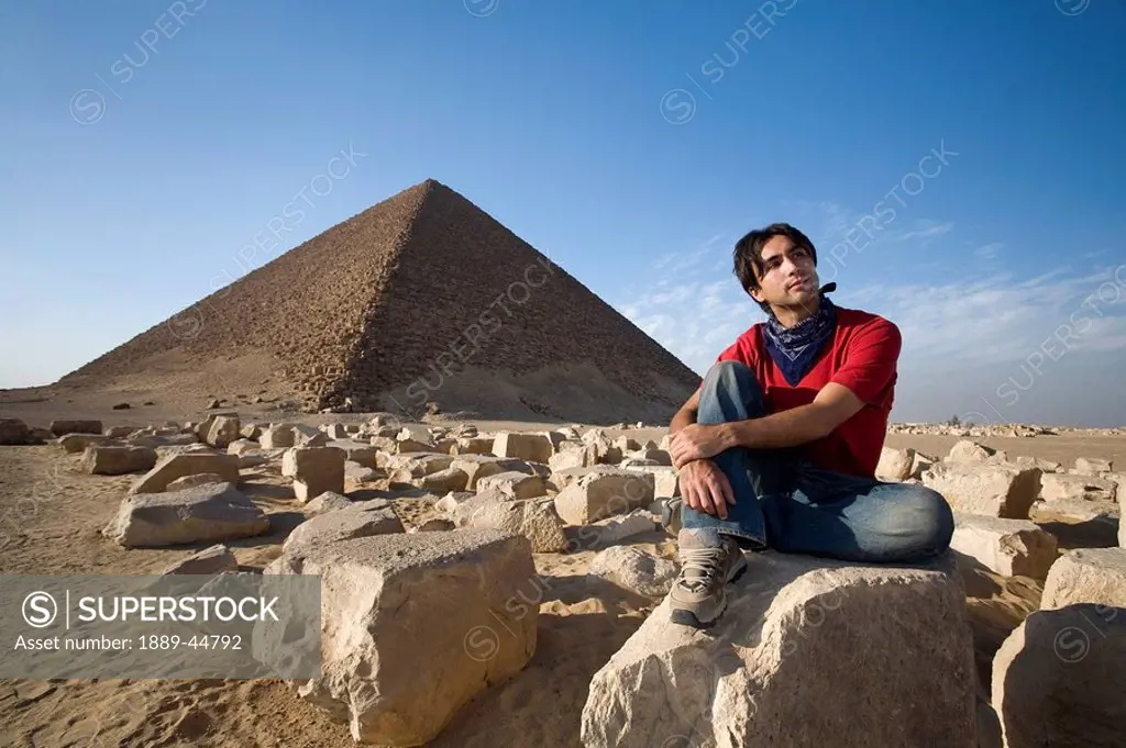 A man sitting near a Pyramid in the desert