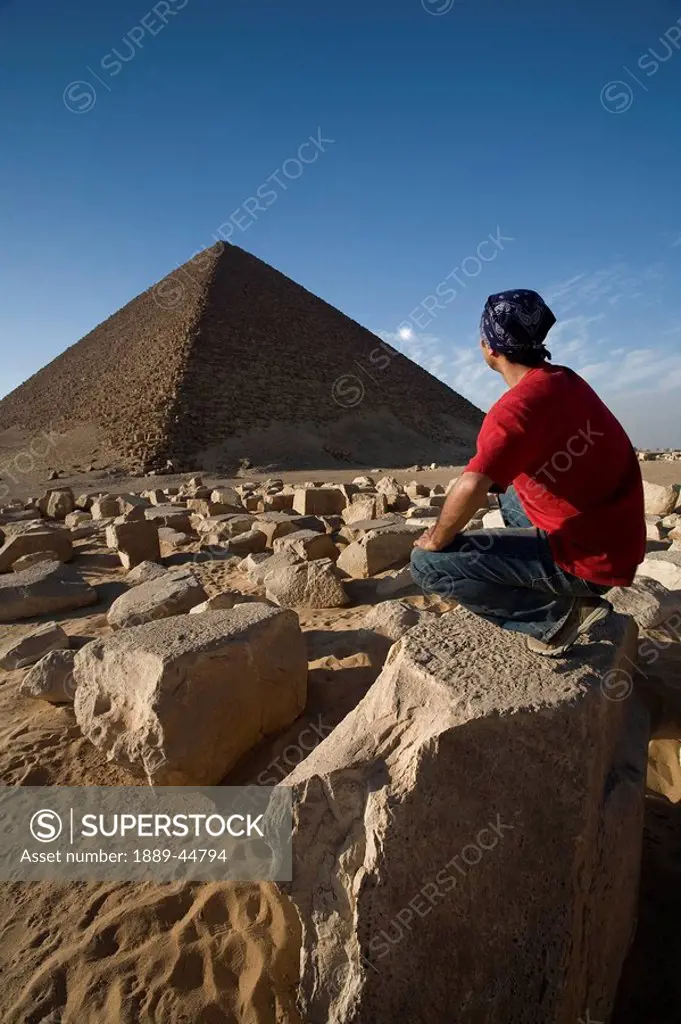 A man crouching near a Pyramid in the desert
