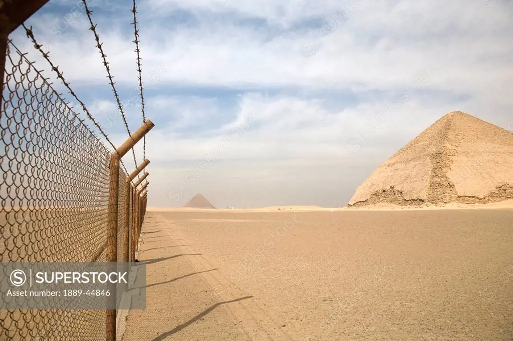 A barbed wire fence by the Bent Pyramid with Pyramid of Giza in background